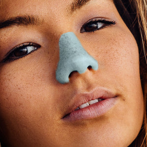 A woman with light blue Nöz sunscreen applied to her nose.