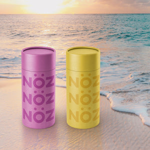 Two Nöz sunscreens (purple and yellow) on the beach.